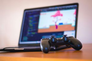 An image of a game controller beside a laptop with coding on it.